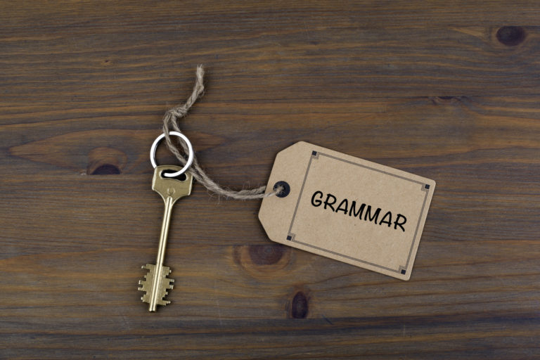 Key and a note on a wooden table with text - Grammar