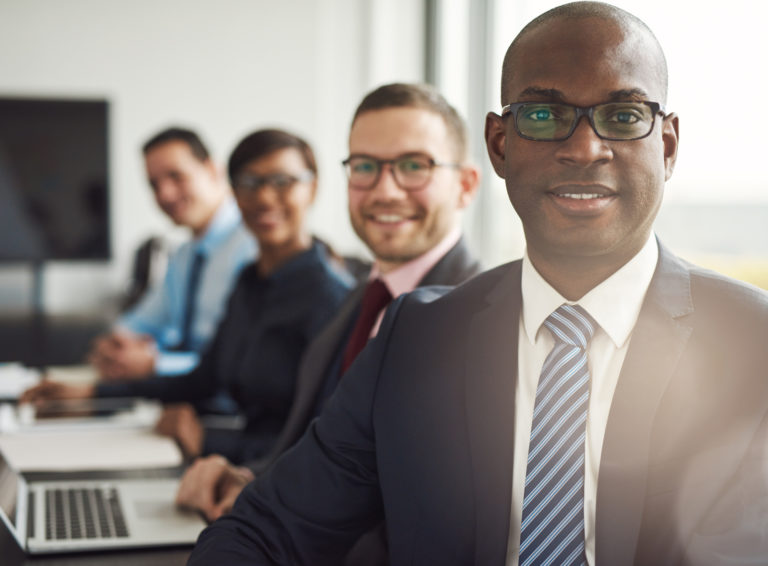 Friendly confident African businessman in a management meeting with a group of multiracial colleagues smiling at the camera
